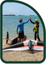 Beginner wing class high five on the beach with foil and wing on the sand