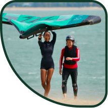 Female walking upwind with a wing giving a class to a female beginner winger