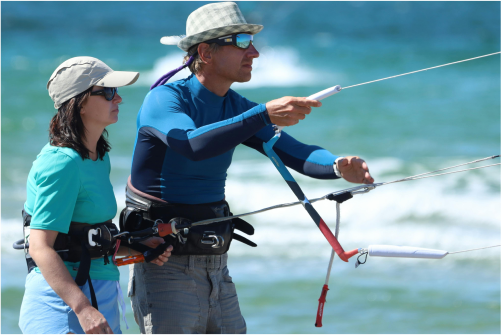 Kitesurf instructor teaching a beginner woman how to water relaunch the kite holding a control bar