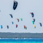 Beach full of kitesurf schools doing kitesurfing lessons.