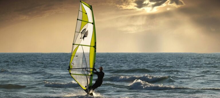 Windsurfer gracefully carving through calm blue waters with a vibrant sail catching the wind."