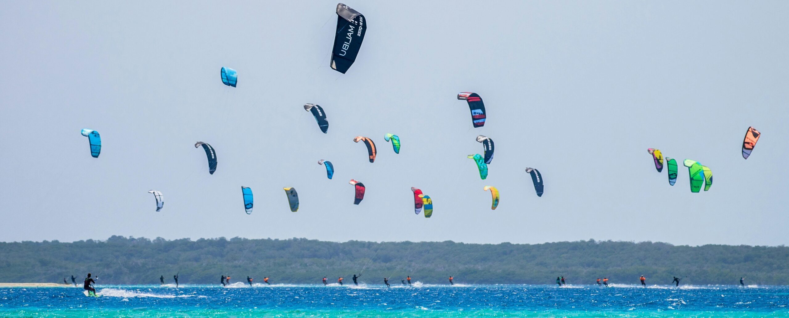 Beach full of kitesurf schools doing kitesurfing lessons.