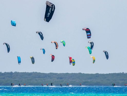Beach full of kitesurf schools doing kitesurfing lessons.